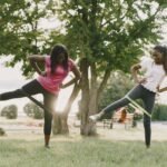 Two women exercising outdoors with resistance bands, focusing on lower body strength