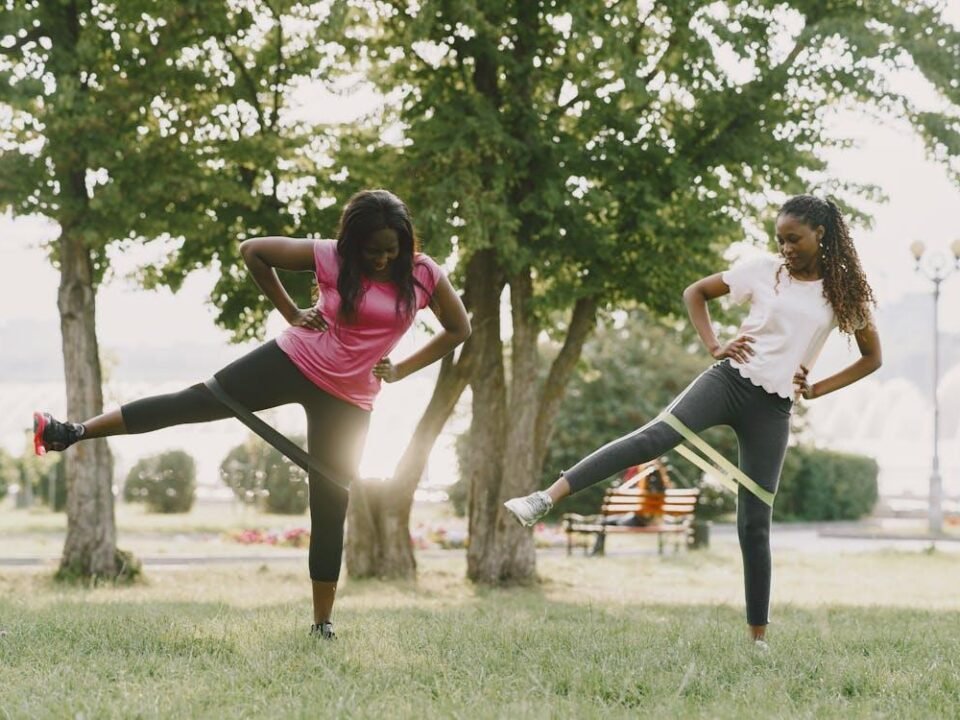 Two women exercising outdoors with resistance bands, focusing on lower body strength
