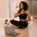 Woman practicing yoga at home following an online fitness class on a laptop